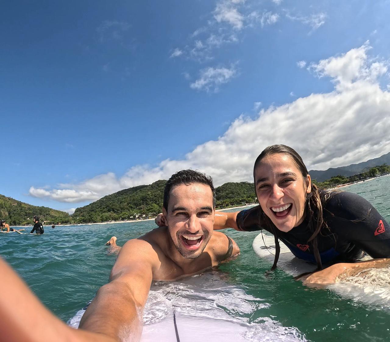 Rachel e Bernardo deitados sobre as pranchas no mar